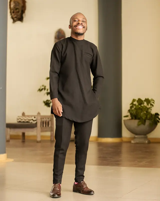 Paddy Daniel standing in a black kaftan in a warm room