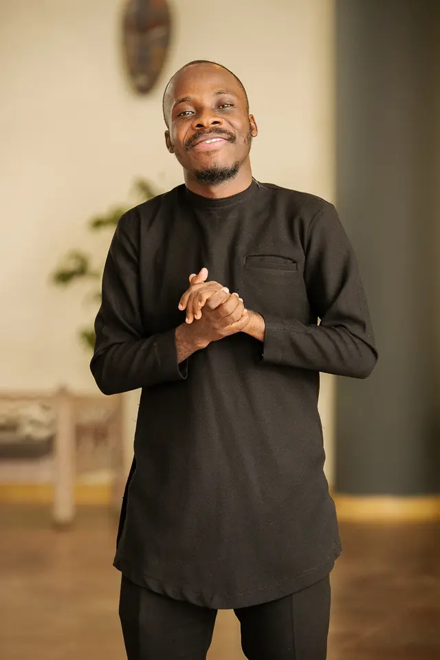 Paddy Daniel in a black kaftan with hands clasped