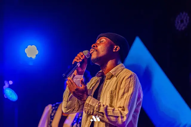 Paddy Daniel singing into a microphone under cobalt stage light